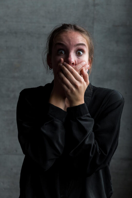 Женщина в черном, закрывающая лицо руками, выражающая страх.